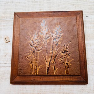 May include: A square, wooden framed artwork featuring a wheat design. The wheat is depicted in shades of gold and light blue against a brown background. The frame is a dark brown color.