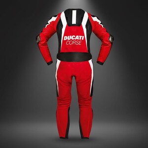 May include: A red and white Ducati Corse racing suit. The suit features black accents, white stripes, and the Ducati Corse logo on the chest. The suit has protective padding on the shoulders and elbows.