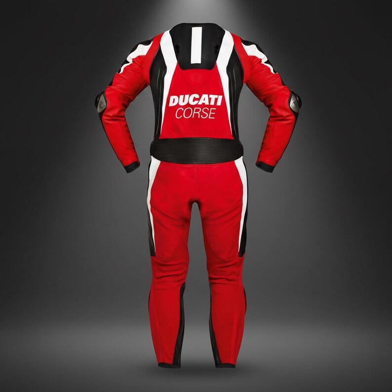 May include: A red and white Ducati Corse racing suit. The suit features black accents, white stripes, and the Ducati Corse logo on the chest. The suit has protective padding on the shoulders and elbows.