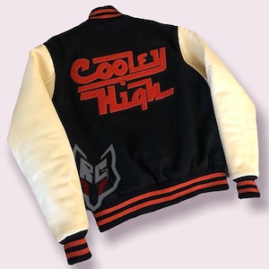 May include: Black varsity jacket with cream sleeves. The back of the jacket features the red text "Cooley High". The jacket has red and orange striped trim on the cuffs, collar, and waist.