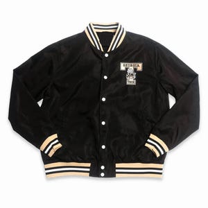 May include: Black satin jacket with white and beige stripes on the collar, cuffs, and hem. The jacket has a button-up front and a patch on the chest that says "Georgia Tech".
