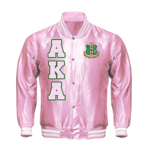 May include: Pink satin varsity jacket with white and green accents. Features the letters "AKA" in green and a crest on the chest. The jacket has a button-up front and white striped cuffs and collar.