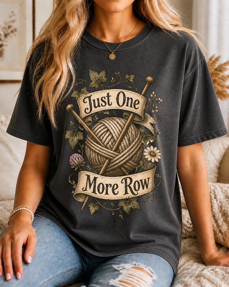 Peut inclure: T-shirt gris fonc&eacute; avec un motif repr&eacute;sentant une pelote de laine, des aiguilles &agrave; tricoter et le texte "Just One More Row". Le motif comprend des &eacute;l&eacute;ments floraux et une banni&egrave;re. Le t-shirt est de style d&eacute;contract&eacute; et confortable.