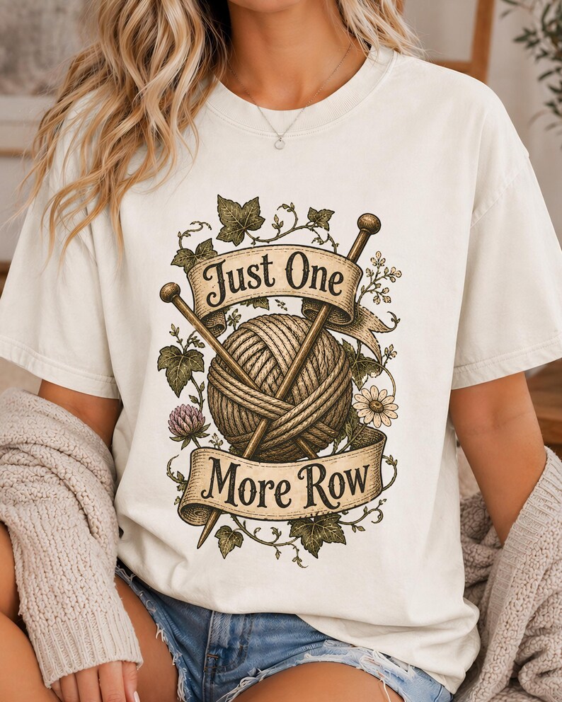Peut inclure: T-shirt cr&egrave;me avec un motif d'une pelote de laine et d'aiguilles &agrave; tricoter, entour&eacute; de motifs floraux et de feuilles. Le texte "Just One More Row" est affich&eacute; sur une banni&egrave;re. V&ecirc;tement confortable et d&eacute;contract&eacute;.