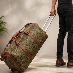 May include: A rolling duffel bag featuring a green and black snakeskin pattern with brown leather straps, a retractable silver metal handle, and wheels. The bag has a cylindrical shape with zippered closures and reinforced leather accents.