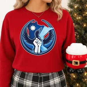 Könnte beinhalten: Ein rotes Sweatshirt mit einem kreisförmigen Grafikdesign in Blau und Weiß. Die Grafik zeigt einen Vogel, eine Faust und einen Stern. Eine Tasse im Weihnachtsmann-Design wird in der Hand gehalten.