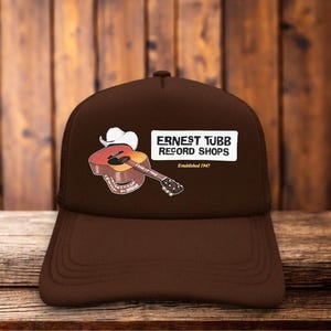 May include: A brown baseball cap featuring a graphic of an acoustic guitar with a white cowboy hat on top. The text reads ERNEST TUBB RECORD SHOPS and Established 1947. The design includes a small guitar illustration with the text ERNEST TUBB.