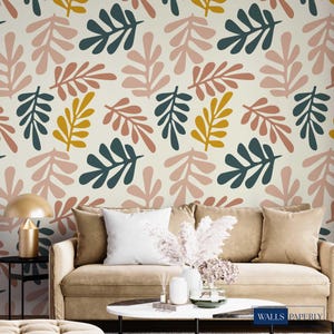 May include: Beige wallpaper featuring a repeating pattern of stylized leaves in pink, teal, and gold. The leaves are arranged in a scattered design. A sofa with cushions and a coffee table are in the foreground.