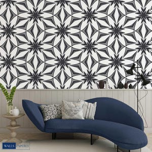 May include: A black and white floral pattern wallpaper covers the wall behind a blue curved sofa. The wallpaper design features repeating star-like shapes. Decorative pillows rest on the sofa. A small side table and a black floor lamp are also visible.
