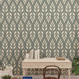 Puede incluir: Papel pintado verde salvia con un patrón repetido de formas cremosas en forma de hojas. Un escritorio de color claro con una silla de madera, libros y material de oficina están frente al papel pintado. El texto "WALLS PAPERLY" está en la parte inferior.