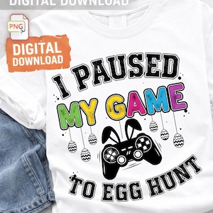 Könnte beinhalten: Weißes T-Shirt mit dem Text "I PAUSED MY GAME TO EGG HUNT" in Schwarz, mit farbigen Akzenten. Ein schwarzer Gamecontroller mit Hasenohren und Ostereiern, die darunter hängen. Digitaler Download.
