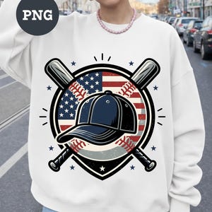 May include: White sweatshirt featuring a baseball-themed graphic. The design includes a baseball cap, baseball bats, and a baseball with the American flag as a backdrop. The graphic is surrounded by stars and a black border.