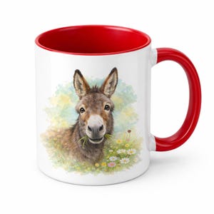 Peut inclure: Mug en céramique blanche avec intérieur et anse rouges. La tasse présente une illustration à l'aquarelle d'un âne mangeant de l'herbe dans un champ de fleurs. L'âne est brun avec de longues oreilles et une expression amicale.