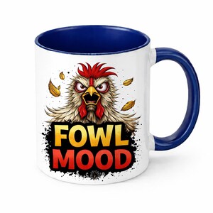 Puede incluir: Taza de cerámica blanca con interior y asa azules. La taza presenta un dibujo de un pollo enfadado y las palabras "FOWL MOOD" en texto amarillo y rojo. El diseño incluye acentos de hojas amarillas.