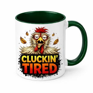 Può includere: Tazza in ceramica bianca con interno e manico verdi. La tazza presenta un disegno di un pollo con la scritta "CLUCKIN' TIRED" in arancione e giallo. Il pollo ha una cresta e un bargiglio rossi ed è circondato da foglie.