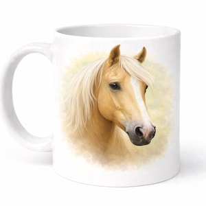 May include: White ceramic mug with a detailed illustration of a Palomino horse's head. The horse has a light tan coat, a white blaze, and a flowing blonde mane. The background is a soft, blurred yellow and green.