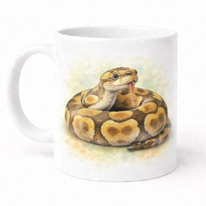 May include: White ceramic mug featuring a detailed illustration of a ball python coiled in a circle. The snake has a tan and brown pattern, with its tongue sticking out. The mug has a white handle and a white background.