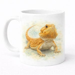 May include: White ceramic mug with a detailed illustration of a bearded dragon. The lizard is shown in orange and brown tones, with a textured appearance. The background has a watercolour effect with blue and yellow hues.