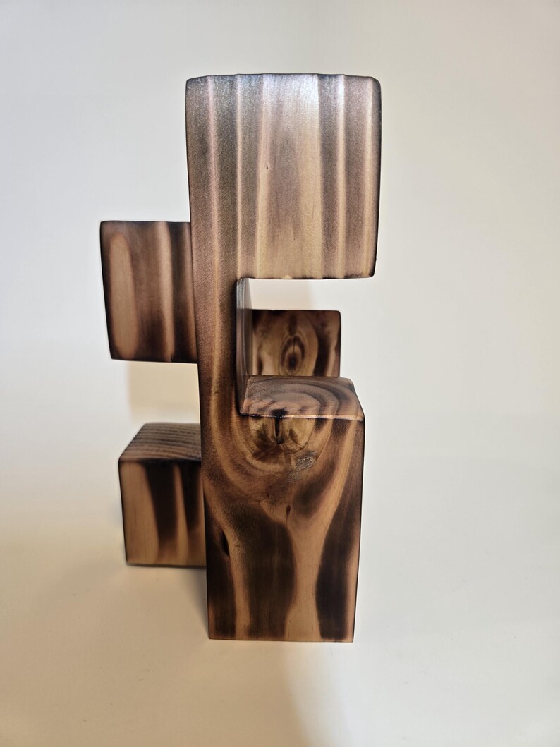 May include: A modern wooden sculpture with a unique, geometric design. The sculpture is constructed from blocks of wood, showcasing a natural wood grain pattern in shades of brown and tan. The piece has a minimalist aesthetic.