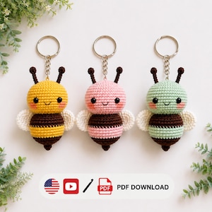 May include: Three crochet bee keychains with metal rings, featuring yellow, pink, and mint green bodies with brown stripes, black eyes, and white wings. The image includes icons for the American flag, a video play button, and a PDF download.
