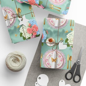 May include: Gift wrap with a teal background featuring a floral and tableware design. The gifts are wrapped with twine and adorned with white tags. A spool of twine, scissors, and blank tags are also present.
