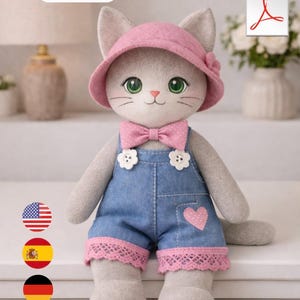 May include: A handmade grey cat doll, 40 cm tall, wearing a pink hat, bow tie, and denim overalls with a pink heart. The overalls have pink lace trim. The doll has green eyes and a pink nose.