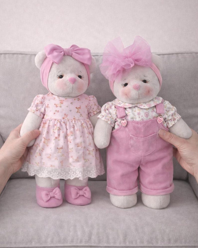 May include: Two plush teddy bears, each with white fur, rosy cheeks, and pink accents. One wears a pink dress and shoes with bows, the other wears pink overalls. Both have pink headbands and bows.
