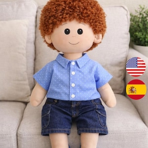May include: A handmade doll, 47 cm tall, with a plush face and curly red hair. The doll wears a blue button-down shirt with white polka dots, denim shorts, and blue shoes. The doll is sitting on a gray sofa.