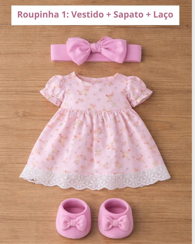 May include: A pink baby outfit set, including a dress, shoes, and headband. The dress features a floral pattern and lace trim. The shoes and headband have bow accents. The text at the top reads "Roupinha 1: Vestido + Sapato + La&ccedil;o".