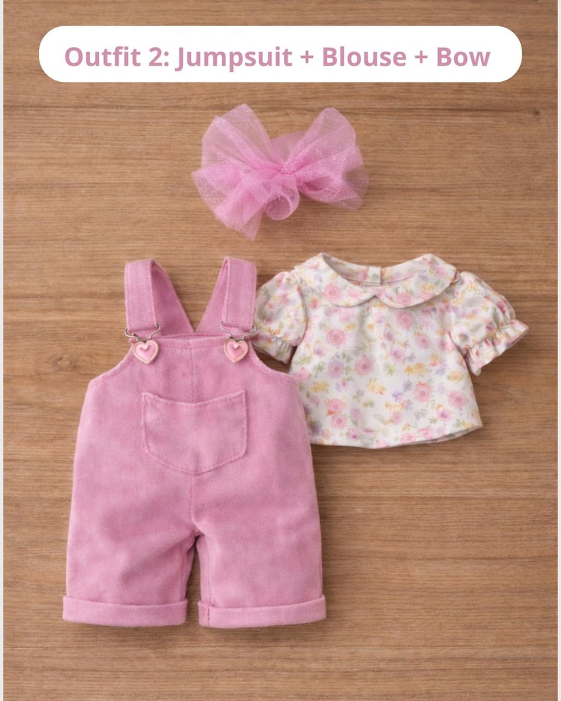 May include: A pink corduroy jumpsuit with heart-shaped clasp details, a floral print blouse, and a pink tulle bow. The outfit is displayed on a wooden surface. Text on the image reads: Outfit 2: Jumpsuit + Blouse + Bow.