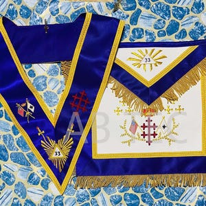 Puede incluir: Un conjunto de collar y delantal masónico azul y dorado. El collar es azul oscuro con ribetes dorados y símbolos bordados. El delantal es blanco con ribetes azules y dorados, flecos dorados y símbolos bordados. El número 33 es visible.