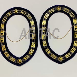 Puede incluir: Dos collares ceremoniales dorados a juego con intrincados diseños geométricos y detalles de estrellas. Los collares están colocados sobre un fondo de terciopelo azul oscuro y conectados por una delicada cadena dorada. El diseño general es simétrico y ornamentado.