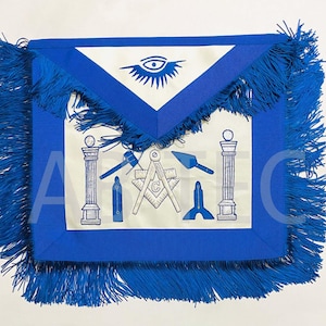 Puede incluir: Delantal masónico azul y blanco con flecos. El delantal presenta un panel central blanco con símbolos masónicos, incluyendo una brújula, escuadra y ojo. El delantal está adornado con flecos azules.