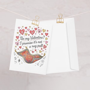 May include: A Valentine's Day card with a red and gold magic carpet illustration, surrounded by hearts and cryptocurrency symbols. The card reads "Be my Valentine? I promise it's not a rug pull" and is paired with a white envelope.