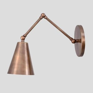 Può includere: Applique da parete color bronzo con paralume conico e braccio regolabile. La base rotonda si monta a parete e il braccio consente l'illuminazione direzionale. L'apparecchio ha un design classico e industriale.