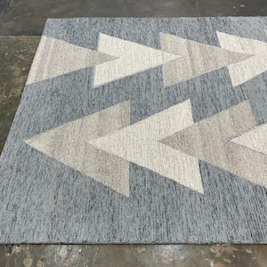 Op de afbeelding: Een rechthoekig vloerkleed met een geometrisch pijlenpatroon. Het vloerkleed heeft een getextureerde, lichtblauwe achtergrond met herhaalde pijlvormen in beige en gebroken wit. Het ontwerp van het vloerkleed voegt een moderne touch toe aan elke ruimte.