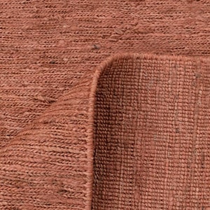 May include: Close-up of a woven rug in a warm, reddish-brown hue. The texture is coarse and appears to be made of natural fibers. The corner of the rug is folded over, revealing the underside.