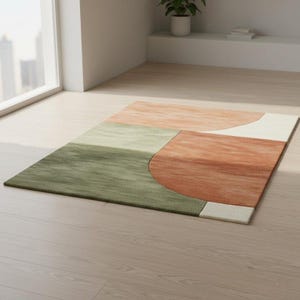 May include: A rectangular area rug with a geometric design. The rug features sections of green, peach, rust, and off-white. The rug is placed on a light-colored wooden floor, near a window.