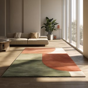 May include: A modern area rug with a geometric design in shades of green, orange, and white. The rug is rectangular with curved and straight edges, and is placed on a hardwood floor in a living room setting.