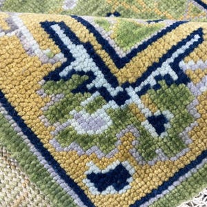 Könnte beinhalten: Nahaufnahme eines Teils eines gewebten Teppichs mit geometrischem Muster. Der Teppich weist eine Kombination aus Farben auf, darunter Gelb, Grün, Blau und Lavendel. Das Design umfasst stilisierte Blumen- und geometrische Formen.