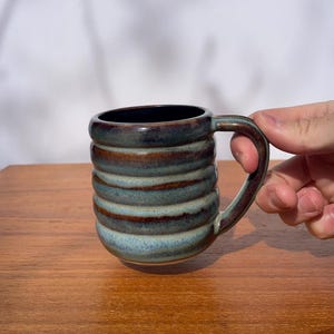 Puede incluir: Un juego de tres tazas de cerámica con un acabado mate moteado. Cada taza presenta un color diferente: azul claro, crema y gris. Las tazas tienen un diseño simple y moderno con una forma redondeada y un asa cómoda.
