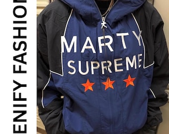 May include: A hooded jacket with a blue and black color block design. The jacket features the text "MARTY SUPREME" in white, with three orange stars below. The brand name "JENIFY FASHION" is printed vertically on the left side.
