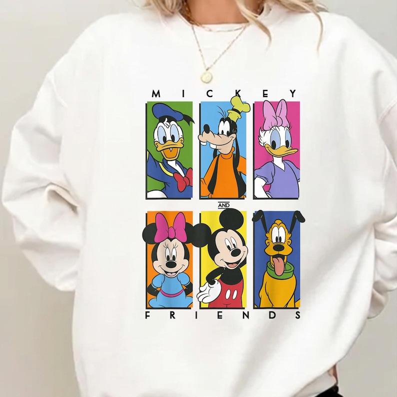 May include: White sweatshirt featuring a colorful graphic of Mickey Mouse and friends. The design includes Donald Duck, Goofy, Daisy Duck, Minnie Mouse, Mickey Mouse, and Pluto, with the words "MICKEY AND FRIENDS" printed above and below the characters.