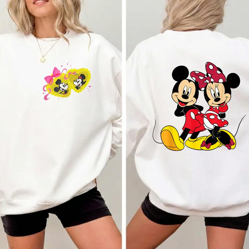 May include: White sweatshirt featuring Mickey and Minnie Mouse. The front displays Mickey and Minnie in a yellow heart with a pink bow. The back shows Mickey and Minnie Mouse in their classic outfits. The sweatshirt is a casual, comfortable style.