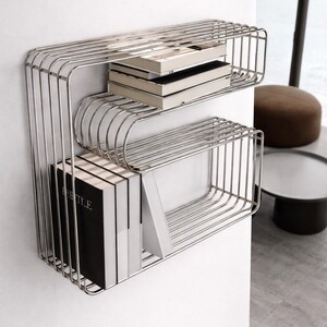 Könnte beinhalten: Ein modernes, zweistöckiges Wandregal aus glänzendem, silberfarbenem Metall. Die Regale sind mit Büchern gefüllt, einige mit schwarzen Einbänden und weißen Seiten. Das Design ist minimalistisch und modern, geeignet für die Inneneinrichtung.