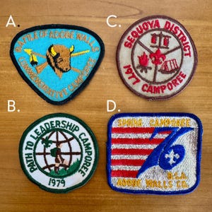 May include: Four vintage embroidered patches. A blue patch with a bison and text, a round patch with text and a figure, a round patch with text and a campfire, and a rectangular patch with red and blue stripes and text.
