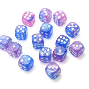 May include: A collection of fifteen six-sided dice featuring a translucent gradient of blue and purple colors with embedded glitter particles and white pips. Each die has rounded corners and displays standard numerical values from one to six.