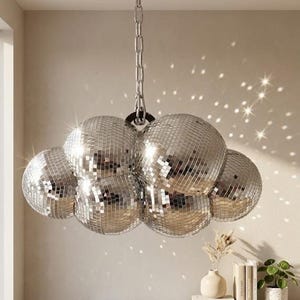May include: A cluster of mirrored disco balls suspended from a ceiling. The silver spheres reflect light, creating a sparkling effect. The fixture hangs from a chain, adding a touch of retro glamour to the room. The overall design is a statement piece.
