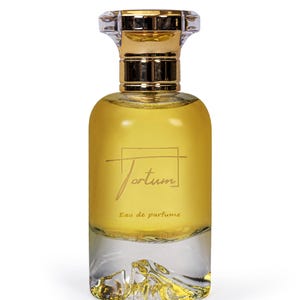May include: A perfume bottle with a clear, textured base and a golden liquid. The bottle has a gold-colored top and a clear, faceted stopper. The word "Jortum" is written on the front, along with "Eau de parfum".