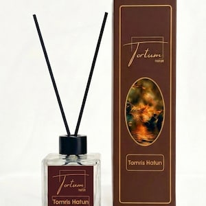 May include: A clear glass diffuser bottle with black reeds and a matching box. The bottle and box are labeled "Jortum Parfum Tomris Hatun". The box features an oval image of a water scene with leaves.